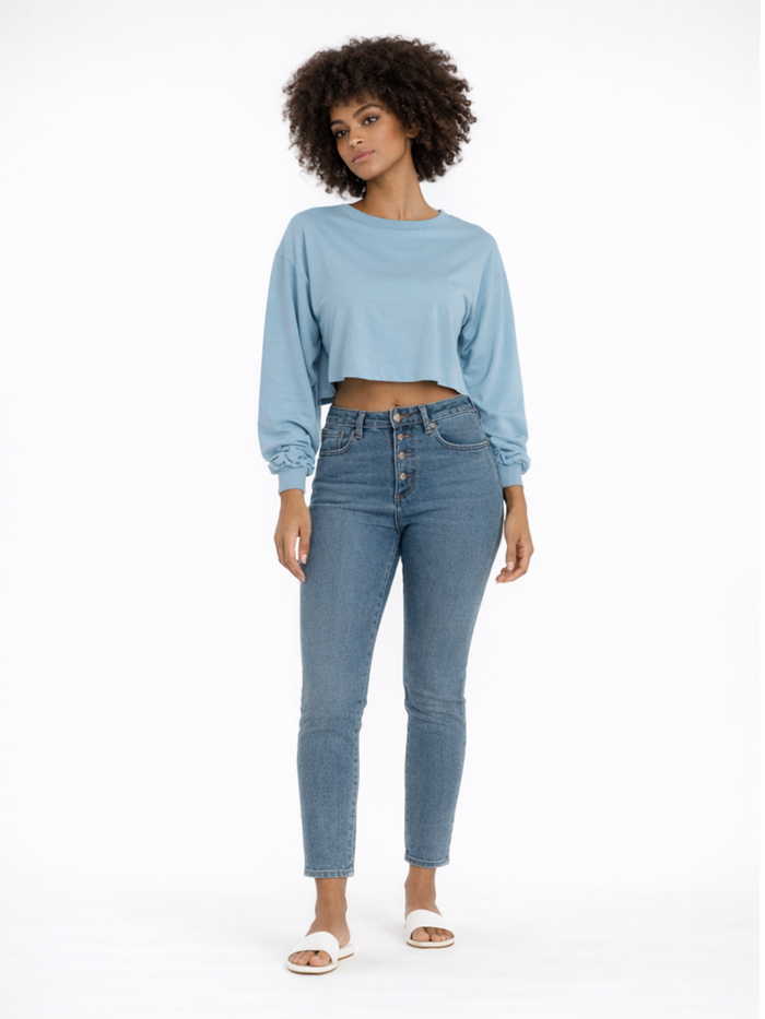 A model poses in a light blue cropped long-sleeve top paired with high-waisted denim jeans and white sandals.
