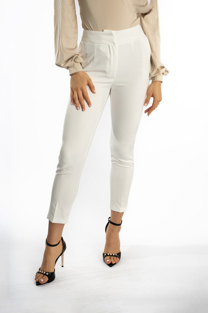 Maisie high-waisted white slim-fit trousers paired with a beige blouse and black pearl-studded heels.
