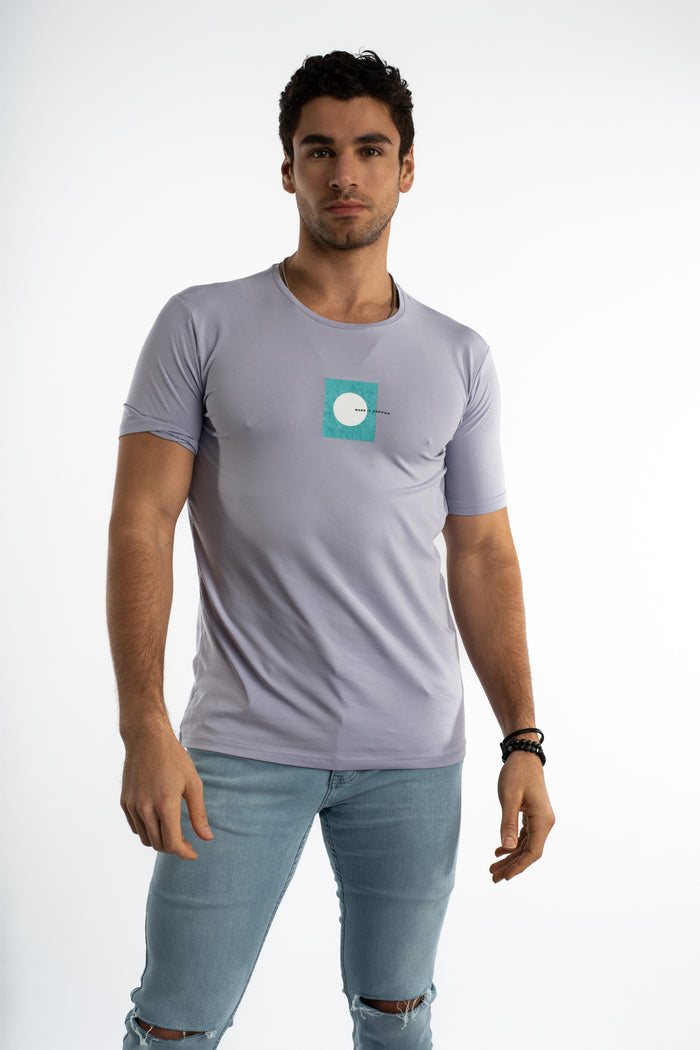Man in lilac Make It Happen graphic streetwear tee and light wash denim jeans, urban fashion aesthetic.