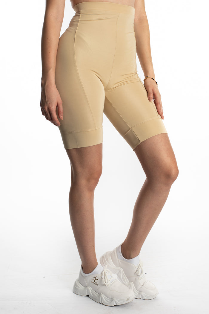 Mara high-waisted beige biker shorts with a seamless fit and wide waistband, paired with white chunky sneakers.