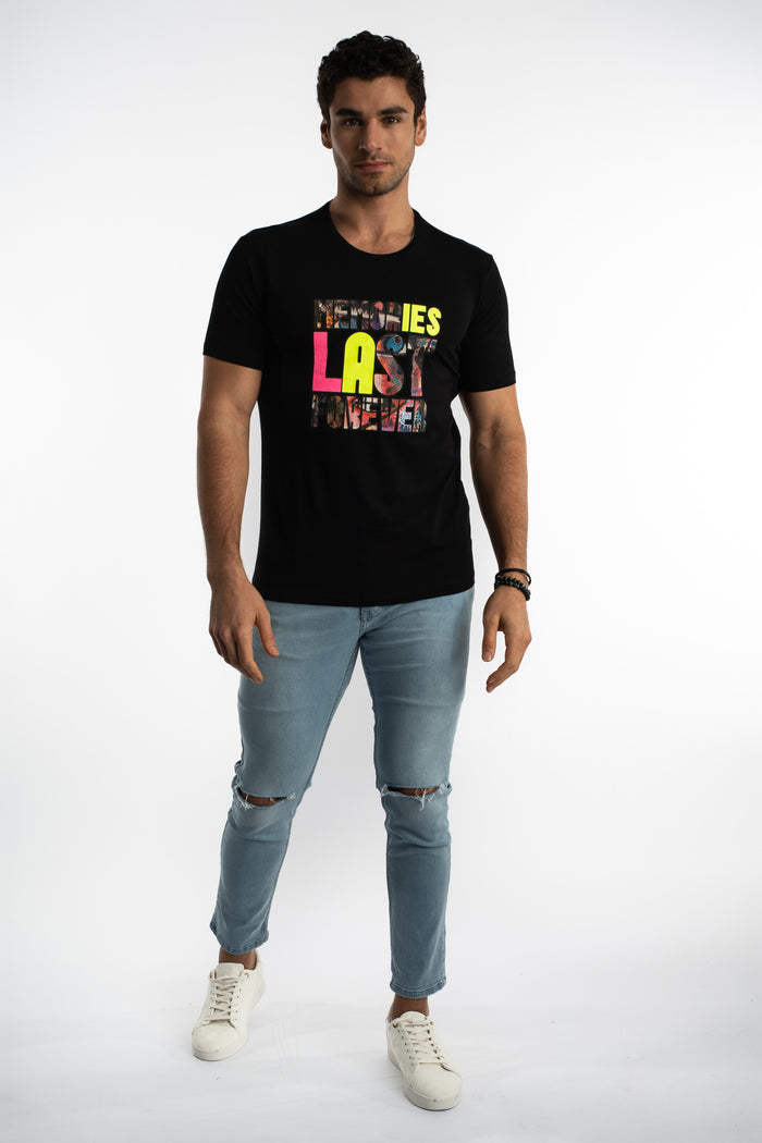 Man in Carbon Memories Graphic T-Shirt in black with streetwear print, light wash ripped denim, and white sneakers.
