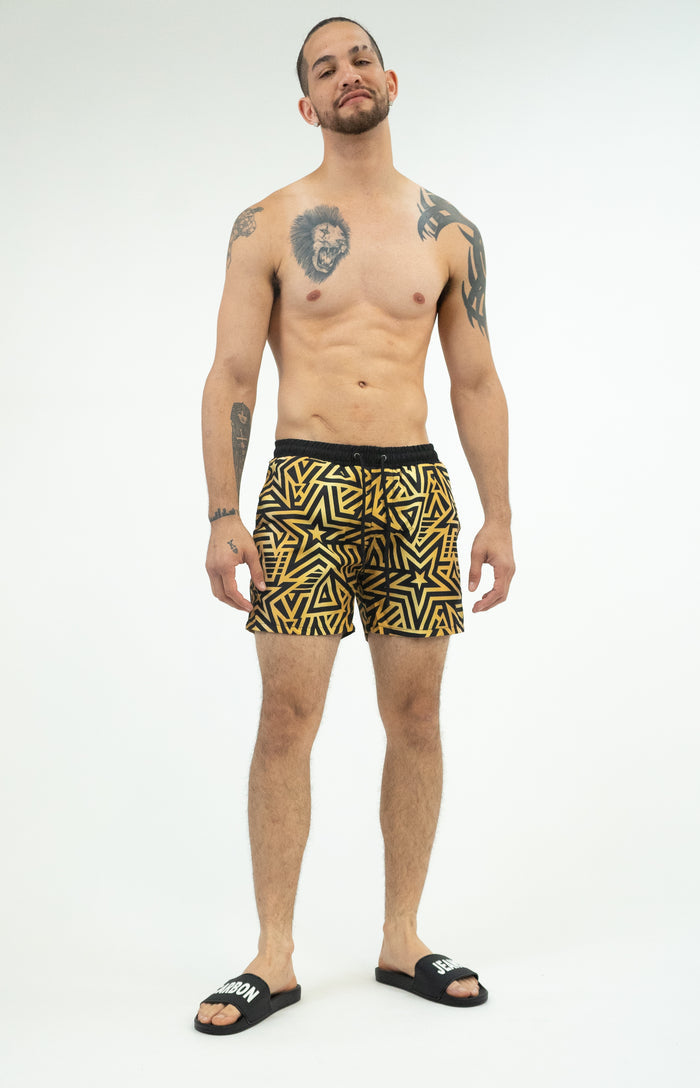Model in Men's Quick-Dry Swim Trunks featuring a black and gold geometric star pattern with drawstring waist.