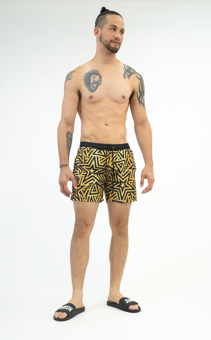 Men’s quick-dry swim trunks in Carbon with black and gold geometric star print on an athletic model.