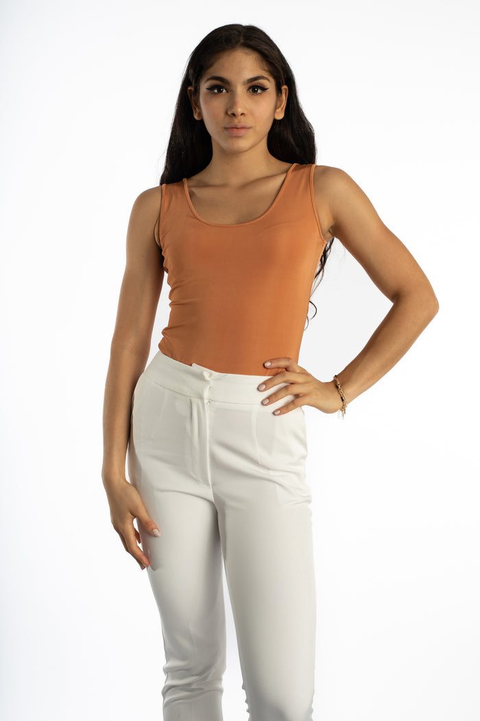 Model wearing the Noa Sleeveless Ribbed Bodysuit in bronze with white trousers against a white background.