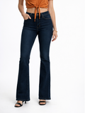 A person wearing a tied orange top and dark flared jeans, standing in black heeled sandals against a white background.