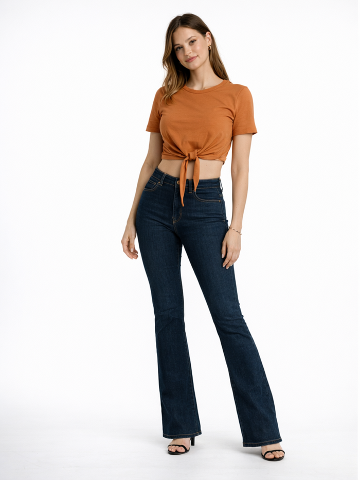A woman poses in a cropped, rust-colored top tied at the waist, paired with dark flared jeans and heels.