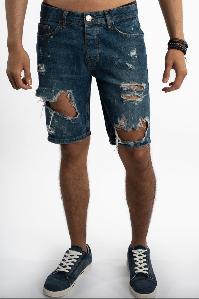 Men’s Otto distressed blue denim shorts with heavy rips, frayed edges, and white paint splatter on a studio model.