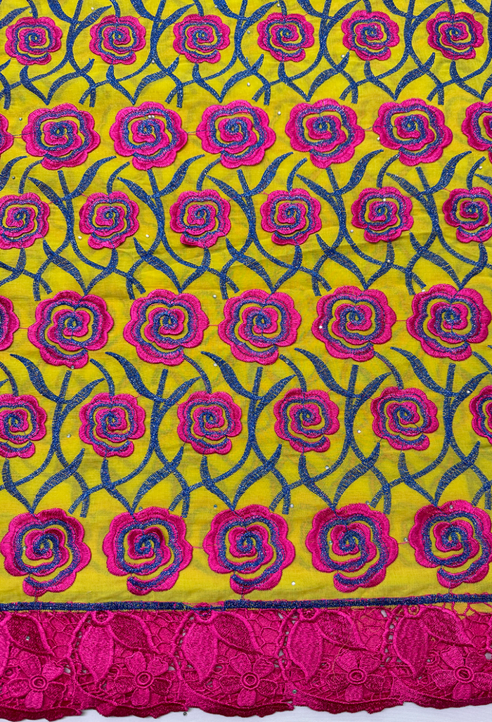 Close-up of Swiss cotton voile lace fabric featuring a pattern with pink and blue floral designs on a yellow background.