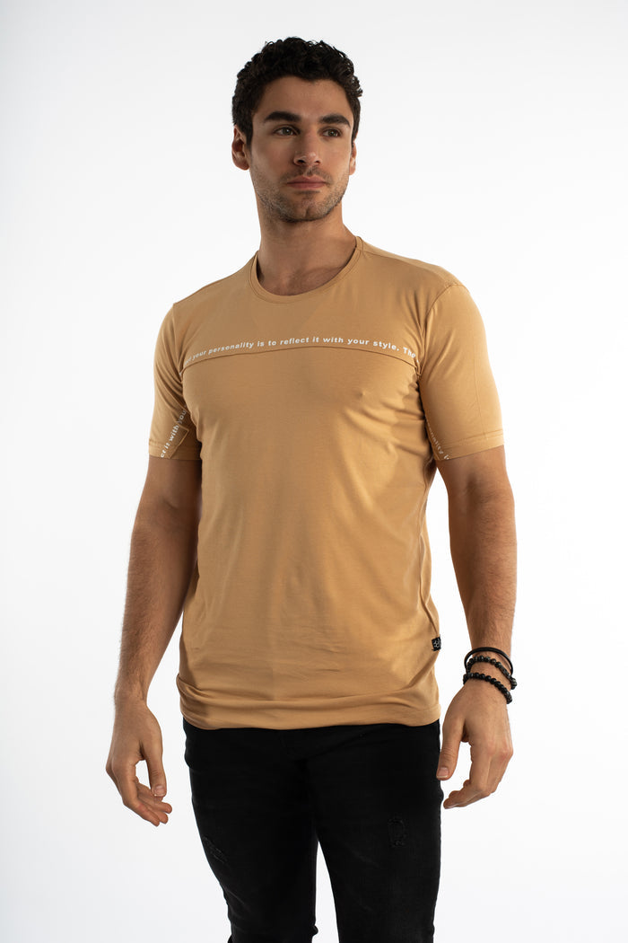 Model wearing the Reflect Your Style streetwear graphic tee in tan with chest text and black slim-fit jeans.