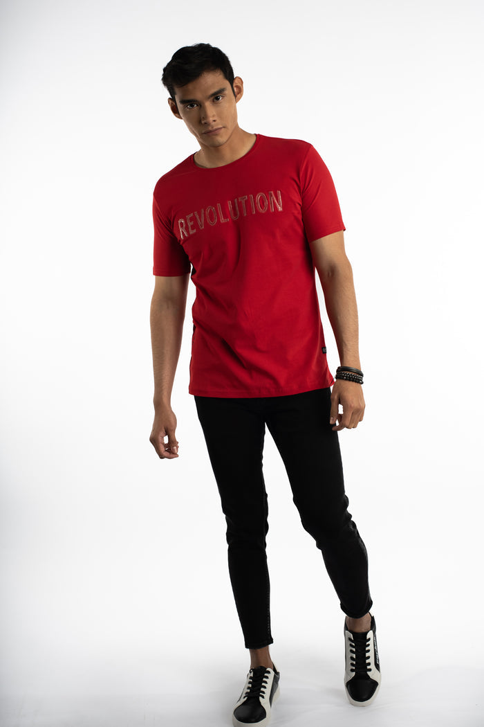 Man wearing a red Revolution graphic tee with embossed metallic text, black skinny jeans, and sneakers for streetwear style.