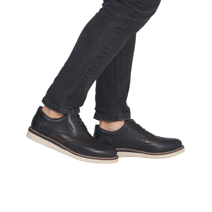 Men's black brogue lace-up leather shoes, worn with dark jeans, cream sole