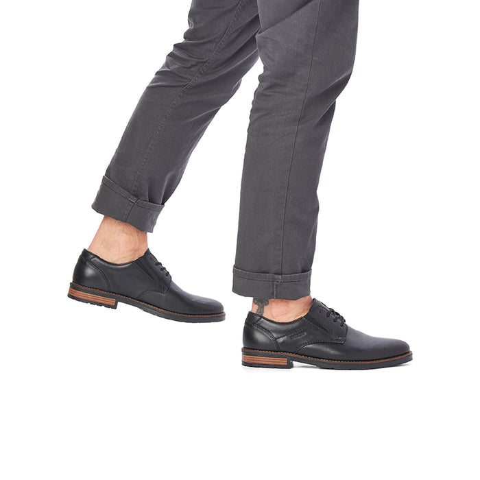 Men's black leather lace-up shoes on feet with gray pants