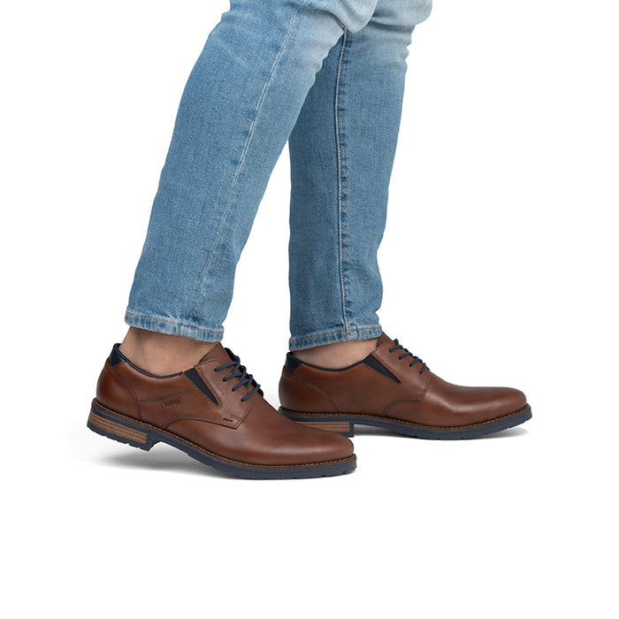 Men's brown leather lace-up shoes on feet with blue jeans