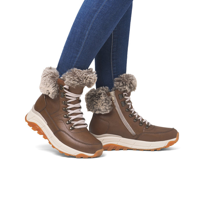 Brown winter snow boot with faux fur cuff, lace-up, and thick sole worn with jeans.