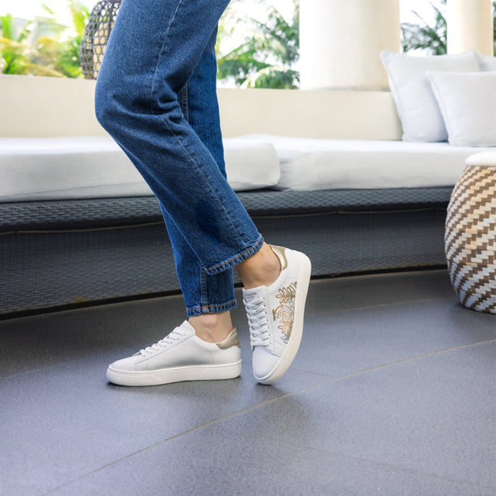 White lace-up sneakers worn with blue jeans on a patio surface.