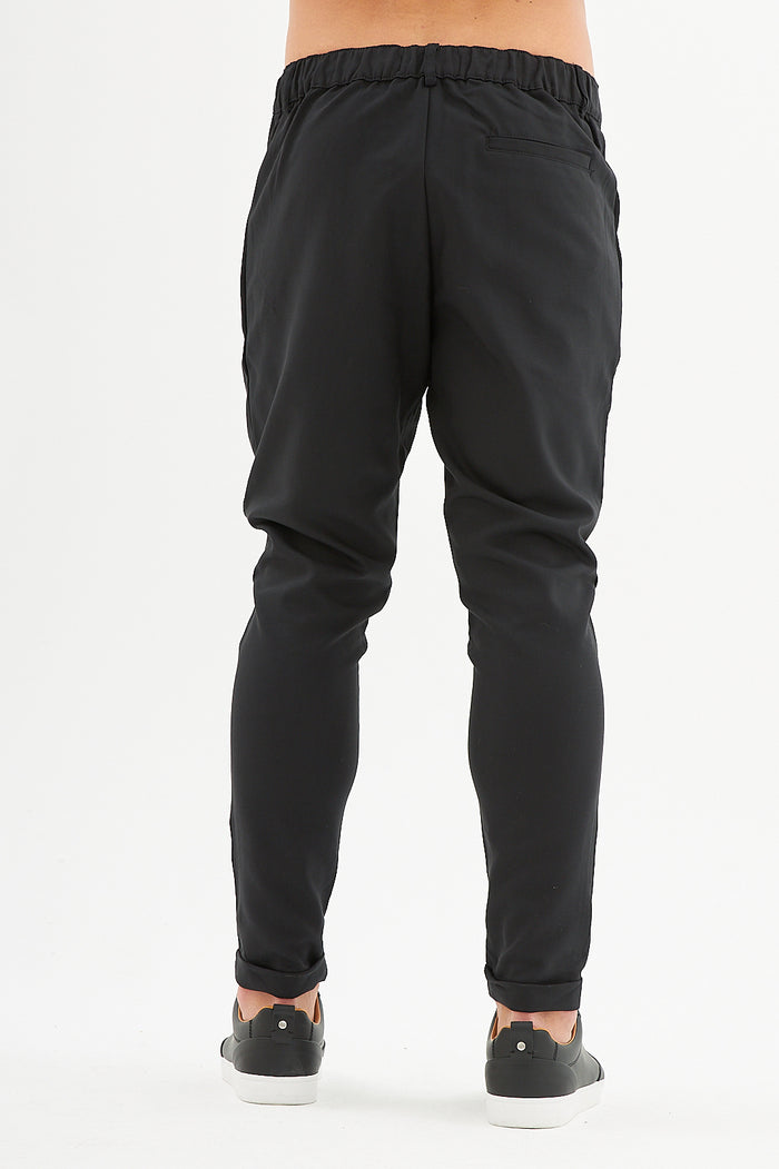 Back view of Ronald slim fit black streetwear pants featuring an elastic waistband and tapered leg on a white background.