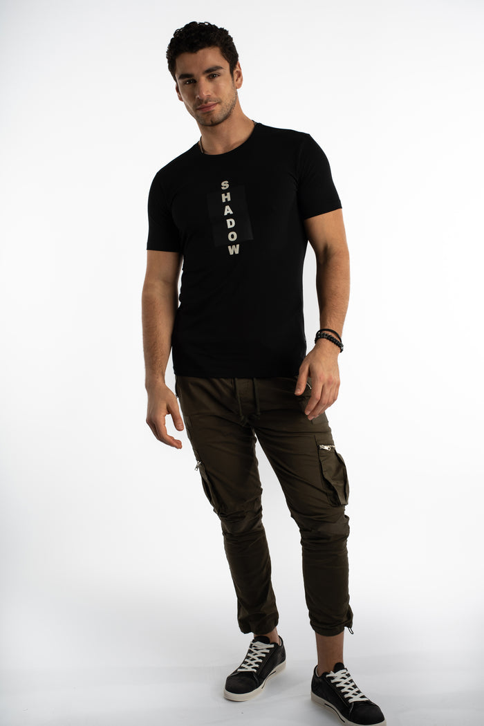 Man wearing Shadow oversized graphic tee in carbon black with olive green cargo pants and black sneakers.