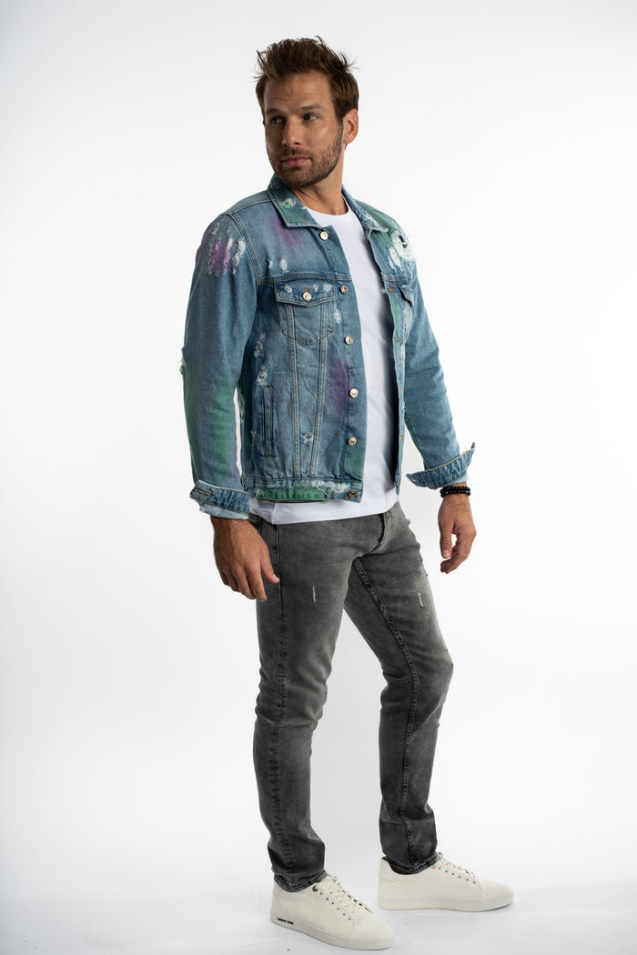 Model in a Stardust distressed denim jacket with purple and green paint splatters over a white tee and grey jeans.