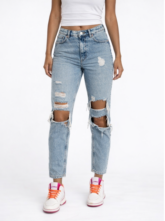 A person wearing distressed light blue jeans with large knee rips, paired with white sneakers and a fitted top.