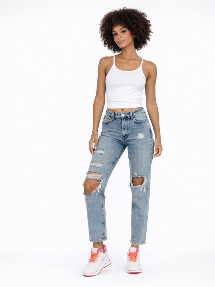 A model poses in a white tank top and distressed blue jeans, paired with white sneakers featuring pink accents.