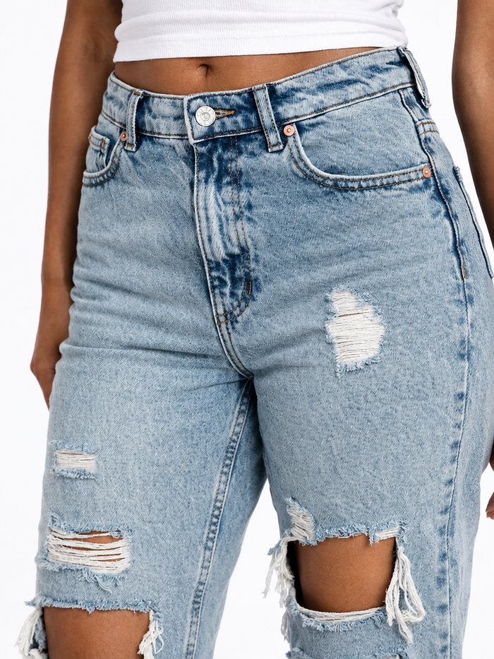 Light blue distressed denim jeans featuring ripped details and a high-waisted fit, styled with a white top.