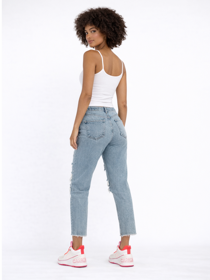 A person with curly hair wearing a white tank top and distressed light blue jeans, standing in casual sneakers.