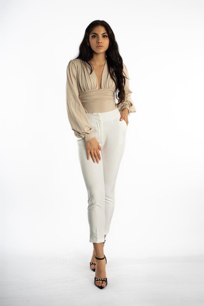 Model in a beige Zuri long-sleeve puff top with a deep V-neck and white tailored trousers for an effortless chic look.